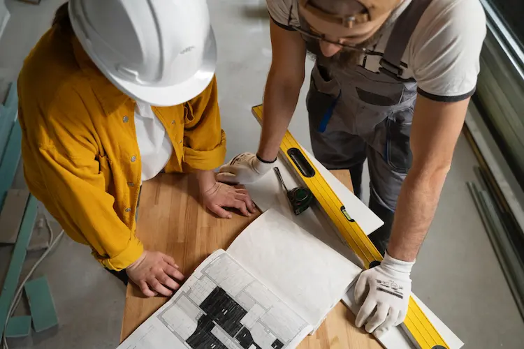 Homme et femme en tenue de chantier avec casque, consultant le plan d’une maison en rénovation énergétique