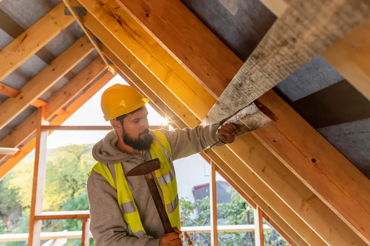 Homme en tenue de chantier inspectant l’isolation des combles d’une maison